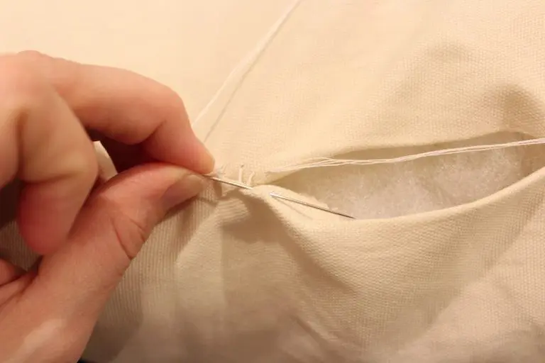 Needle entering the fold of a pillow cover to begin an invisible stitch.