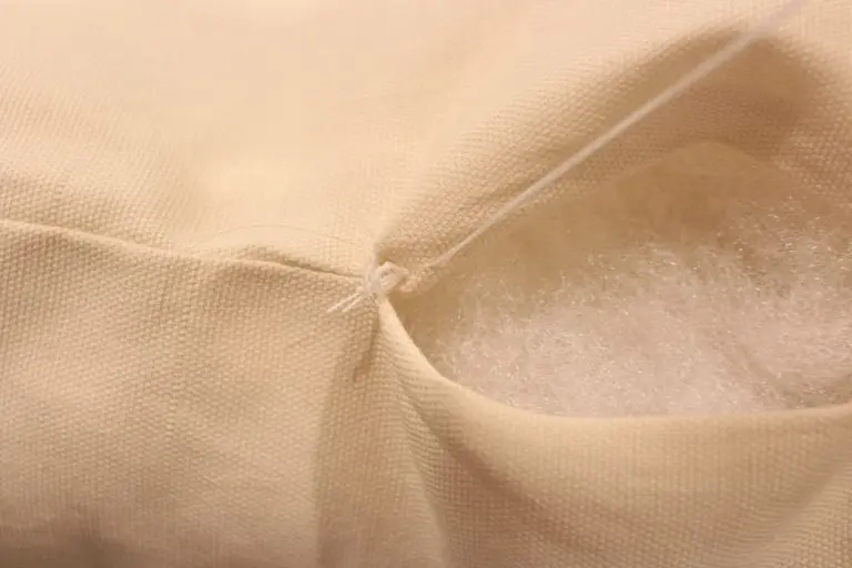 Close-up of hand stitching across a fabric pillow opening with white thread.