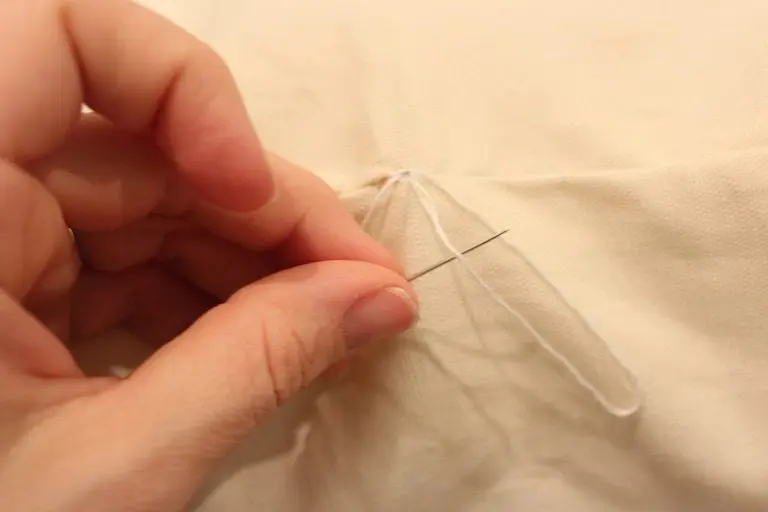 Needle looping through thread to create a knot at the end of a seam.