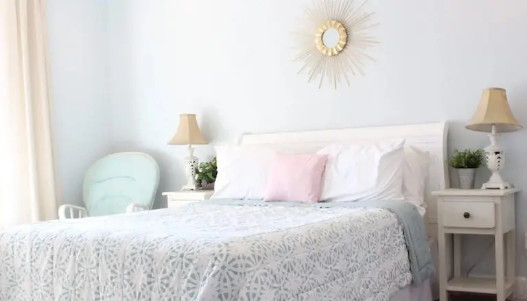 Bright bedroom with white bedframe, patterned quilt, and handmade throw pillows styled with a blush accent pillow.