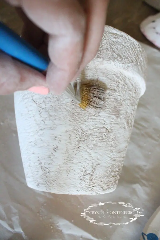 Painting brown paint onto a plaster of paris terra cotta pot