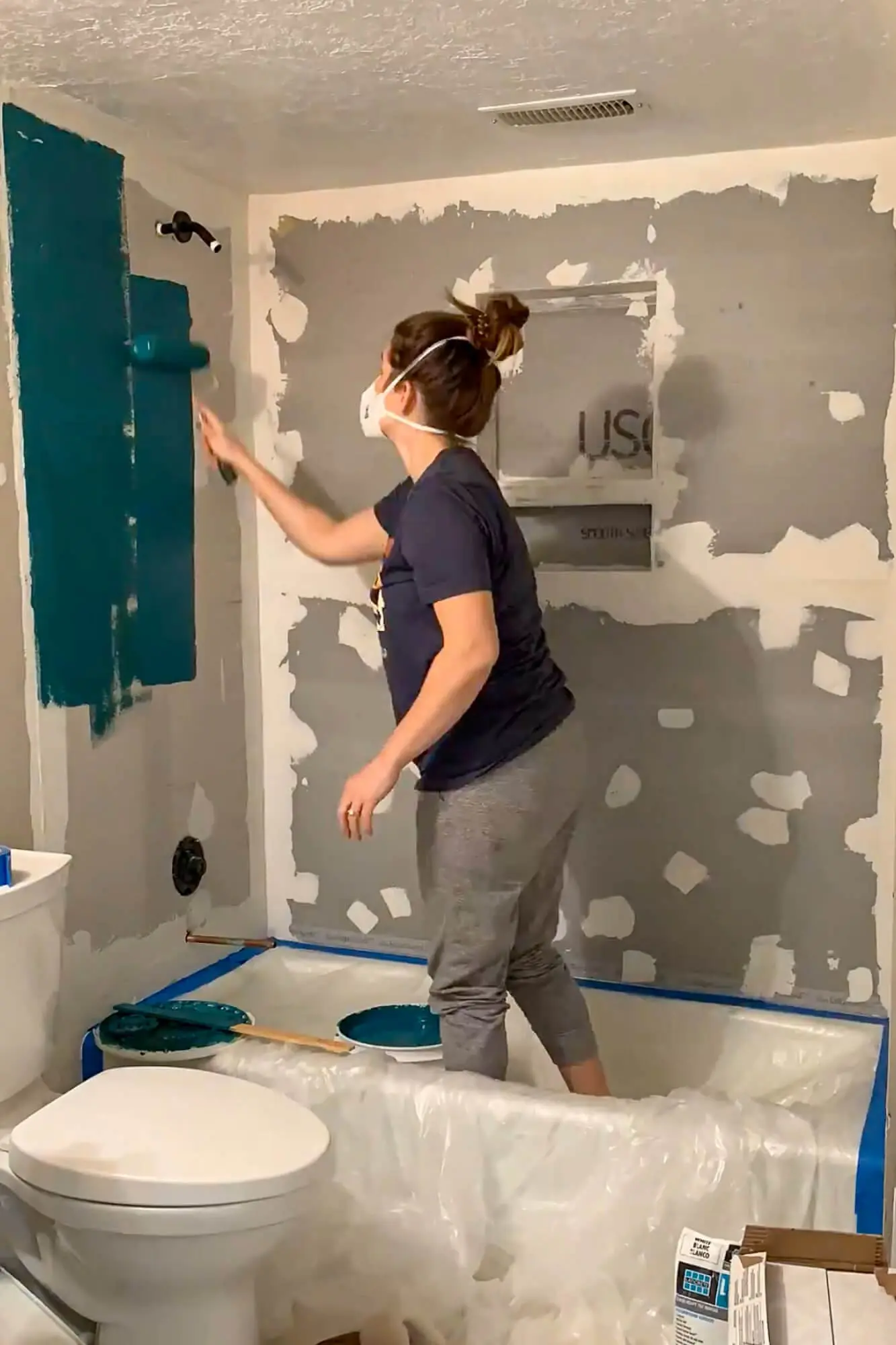 Applying dark green liquid waterproofing membrane over cement board in the shower surround.