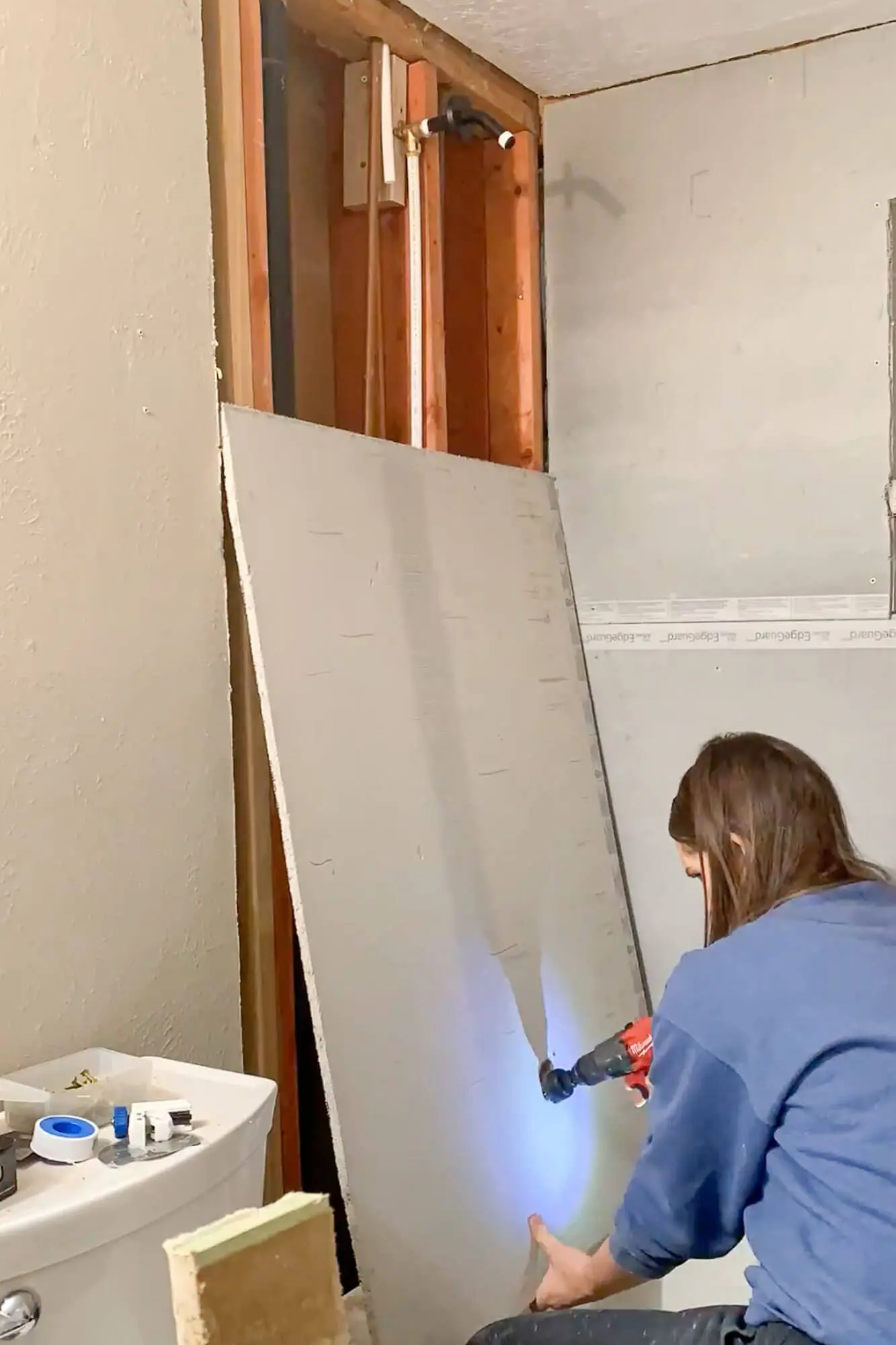 Installing cement backer board over shower studs with cutouts for plumbing and niche.