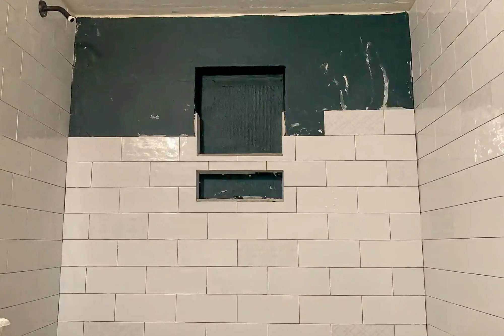 White subway tiles being installed around a double shower niche with decorative patterned tile on the back.
