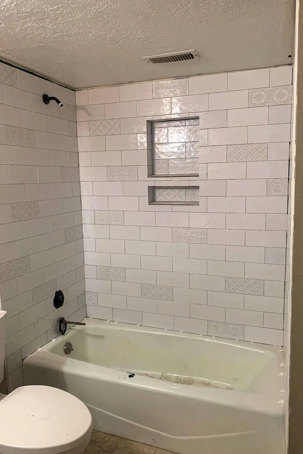 Back wall of shower with double niche and decorative subway tiles.