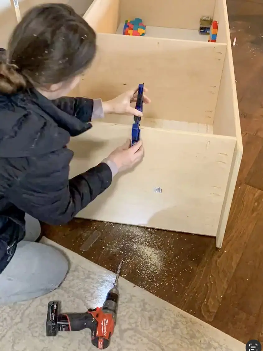 DIYer using a Kreg pocket hole jig to drill precise holes for secure joinery in a built-in office cabinet project.