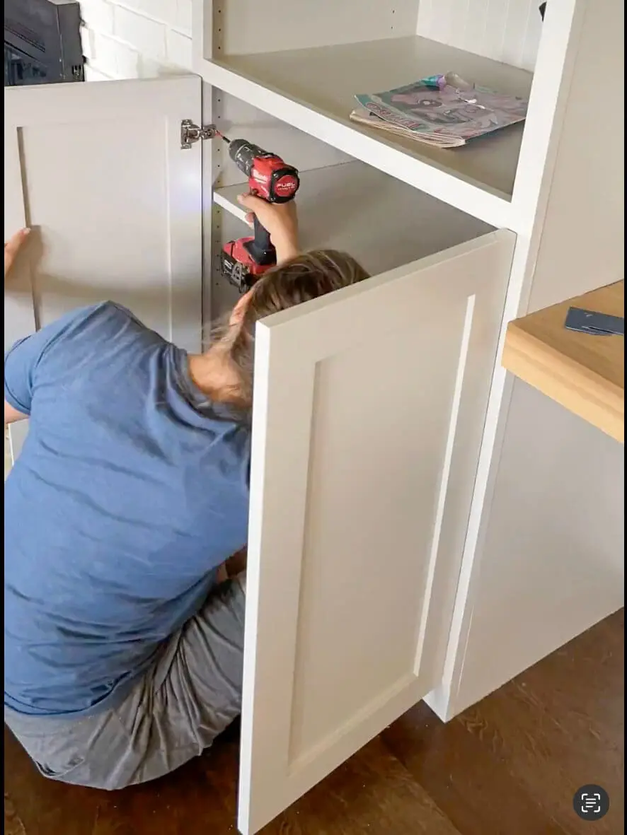Woman installing a white shaker-style cabinet door with a power drill.