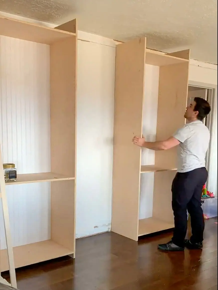 Man lifting and installing a large wooden cabinet as part of a custom built-in office setup.
