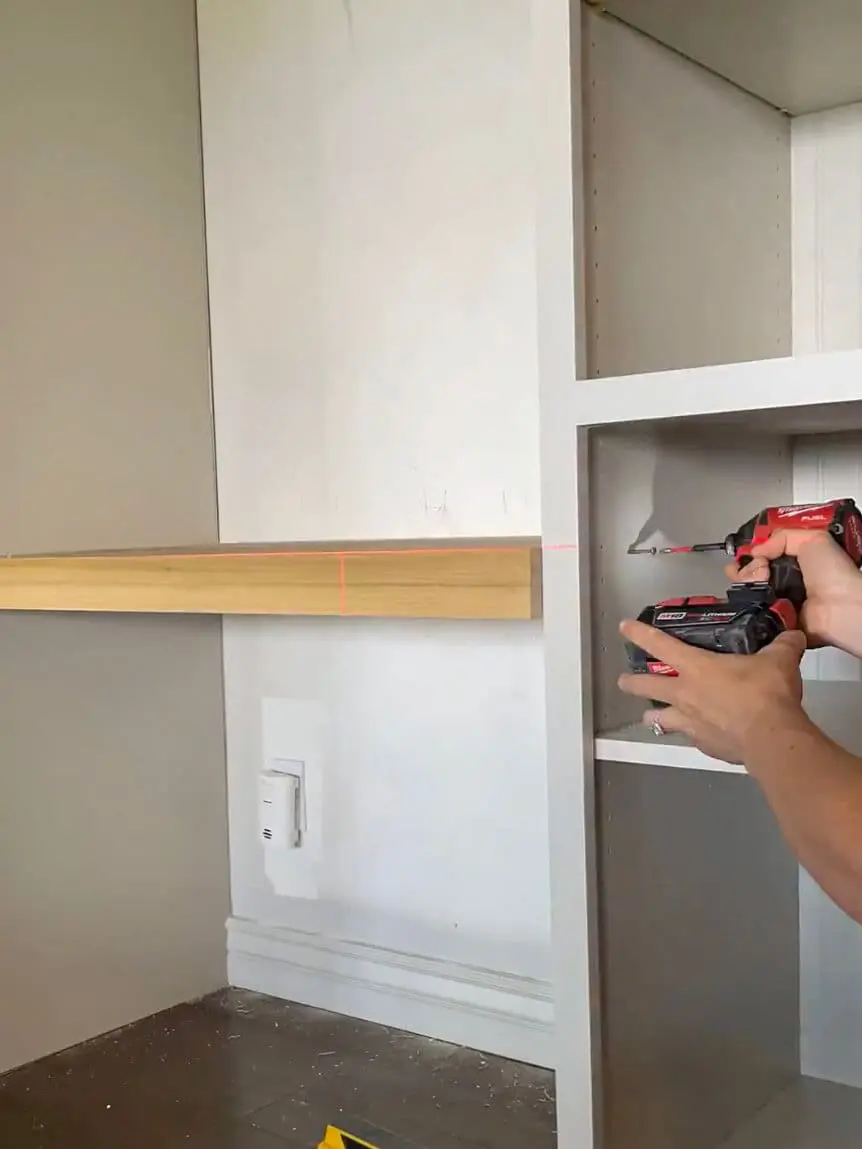 Woman securing a floating wooden desk between built-in office cabinets.
