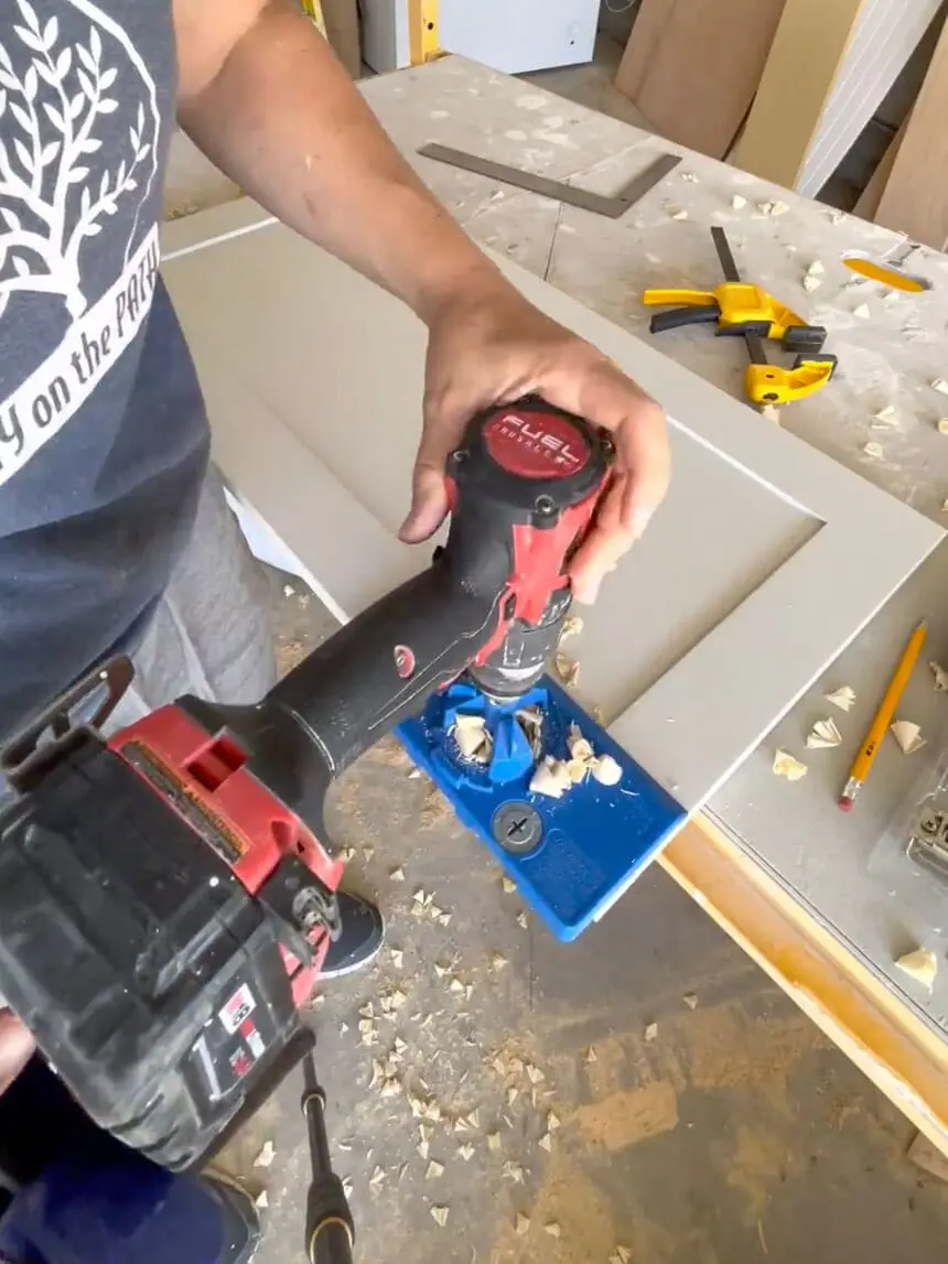 Close-up of a Kreg Jig being used to drill holes for cabinet door hinges.