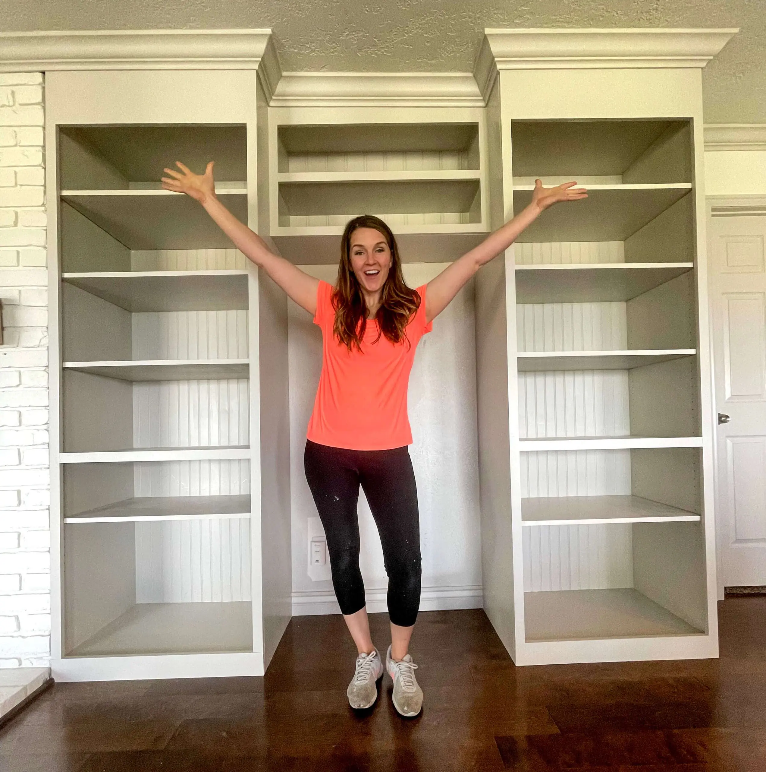Woman standing between two large built-in bookcases, celebrating the nearly finished project.