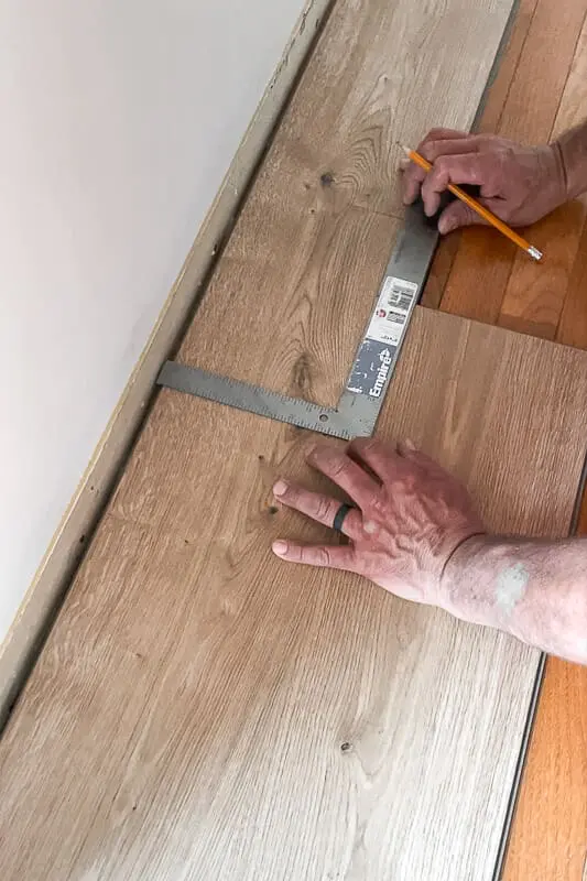 Carpenter square and pencil marking the end cut of a plank before installing against a wall