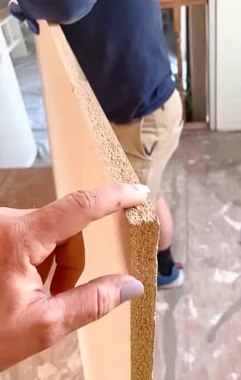 Hand holding a piece of ¾-inch particle board used to raise the floor height for an even plank install.