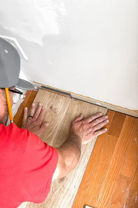 Man in red shirt installing final plank near wall, demonstrating tight seam and no expansion gap