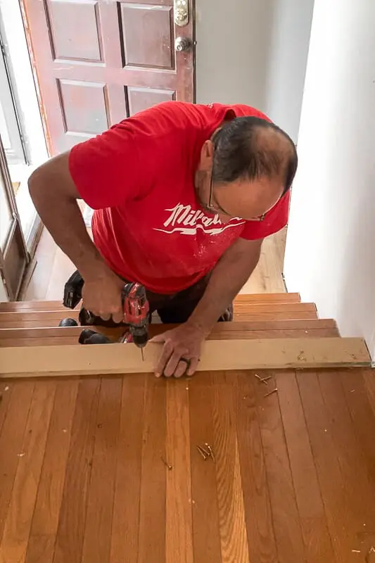 Grandpa screwing down a temporary guide board to help lay the first rows wood floors