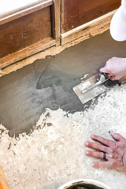 Spreading leveling cement across uneven subfloor to create a smooth surface for floating floors.