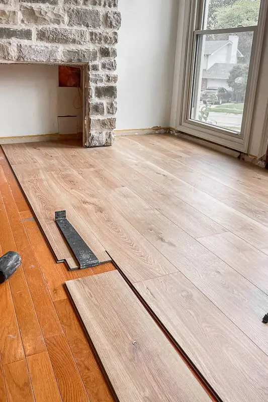 Installing Duravana plank flooring in front of a stone fireplace, mid-project with old wood floors still partially visible.