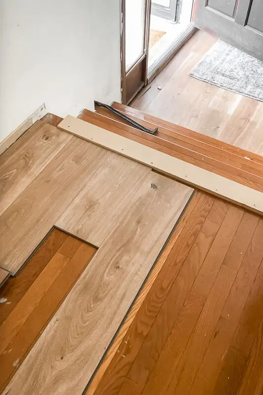 Top-down view of wood plank flooring being installed at the edge of a staircase with guide board in place