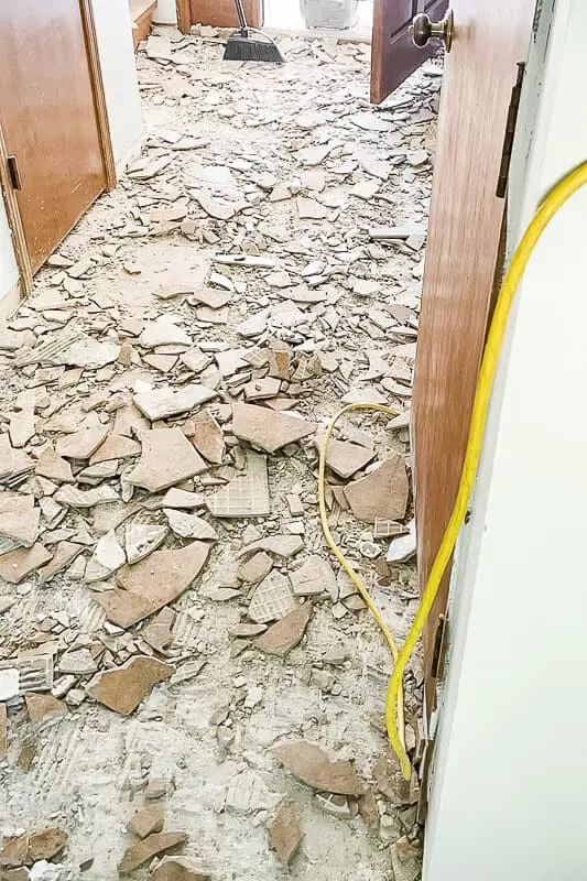 Pile of broken tile scattered across the floor after demolition, showing the messy side of floor prep.