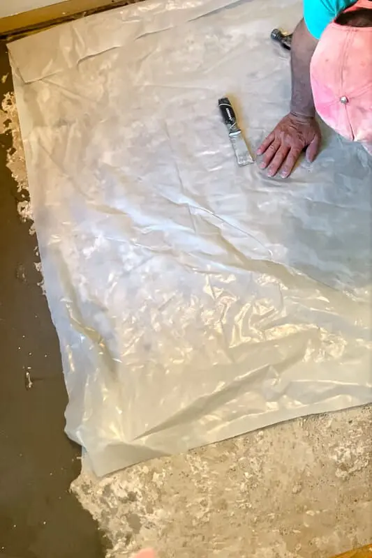 Laying a plastic vapor barrier sheet over concrete subfloor 