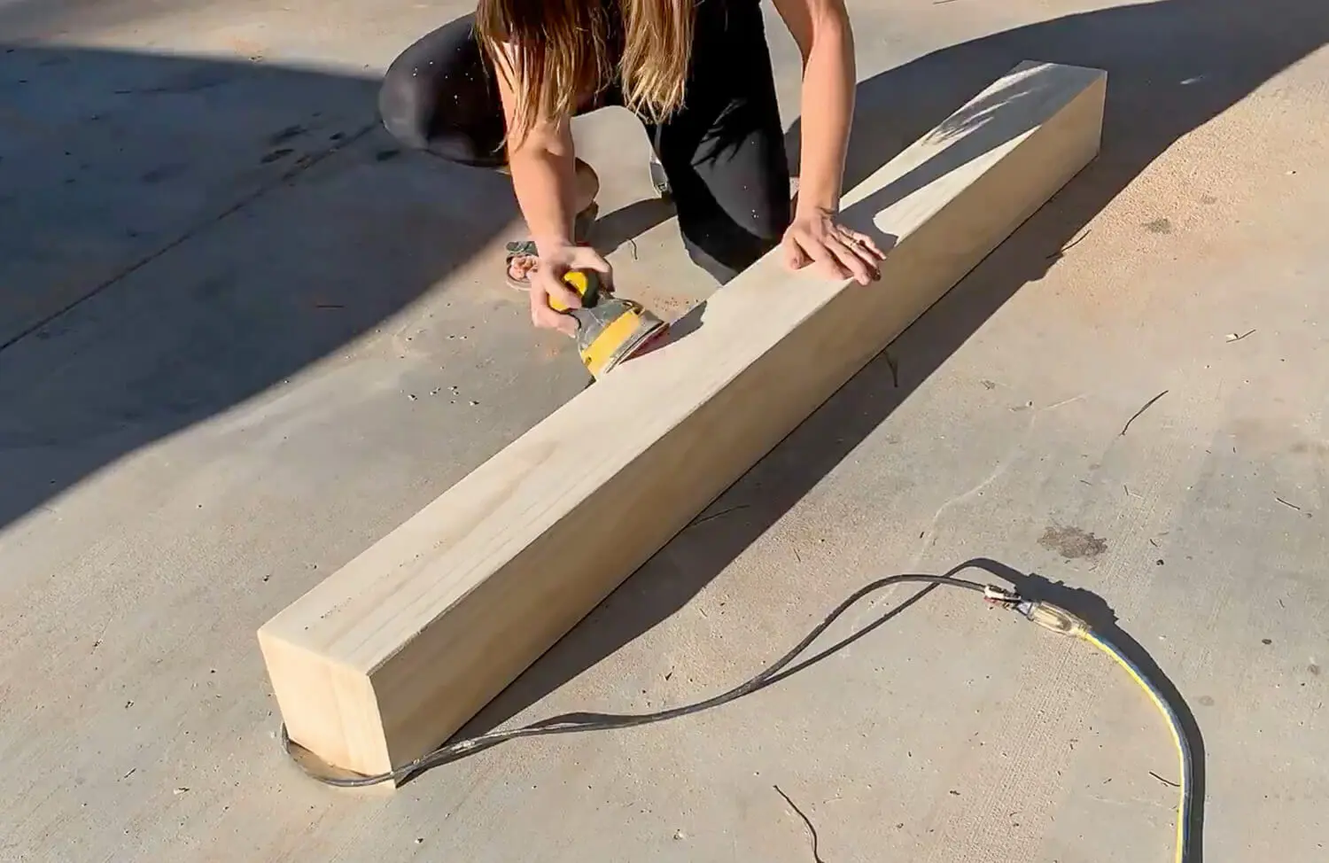 Woman using orbital sander on hollow beam mantel to smooth seams and filler