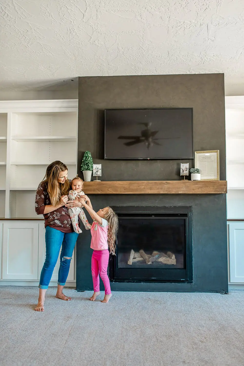 Finished DIY floating mantel installed above black fireplace with built-in shelving