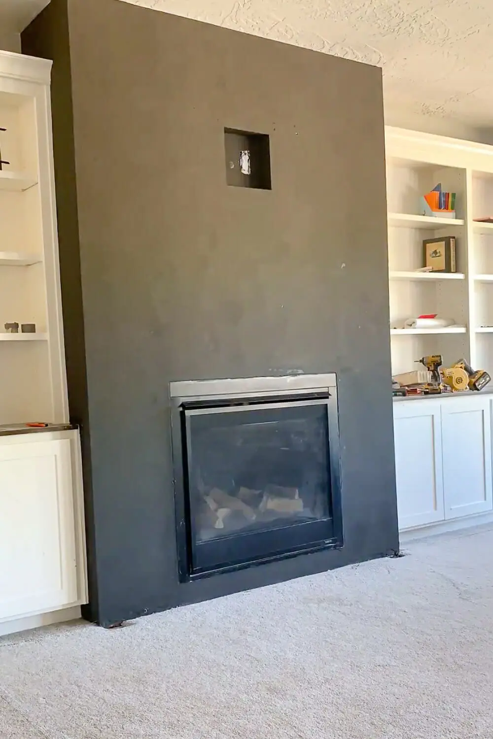 Fireplace with both coats of black textured plaster complete before mantel installation, recessed media box visible, tools on nearby counter