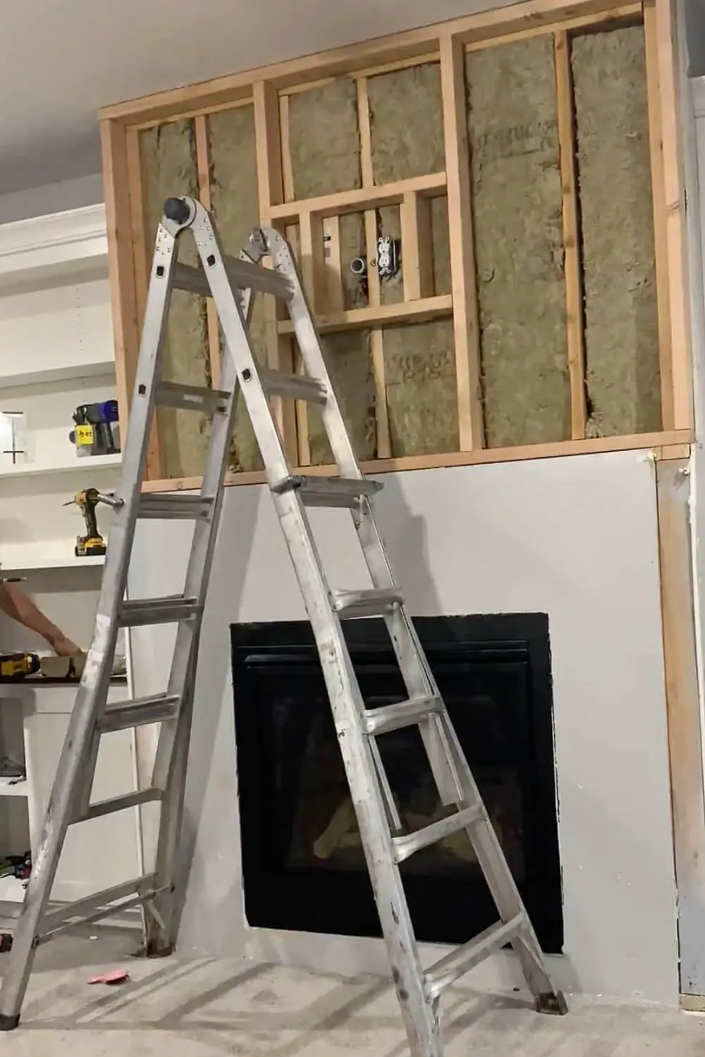 New 2x4 stud wall framing installed above fireplace with insulation visible, electrical outlet for media center, ladder in position