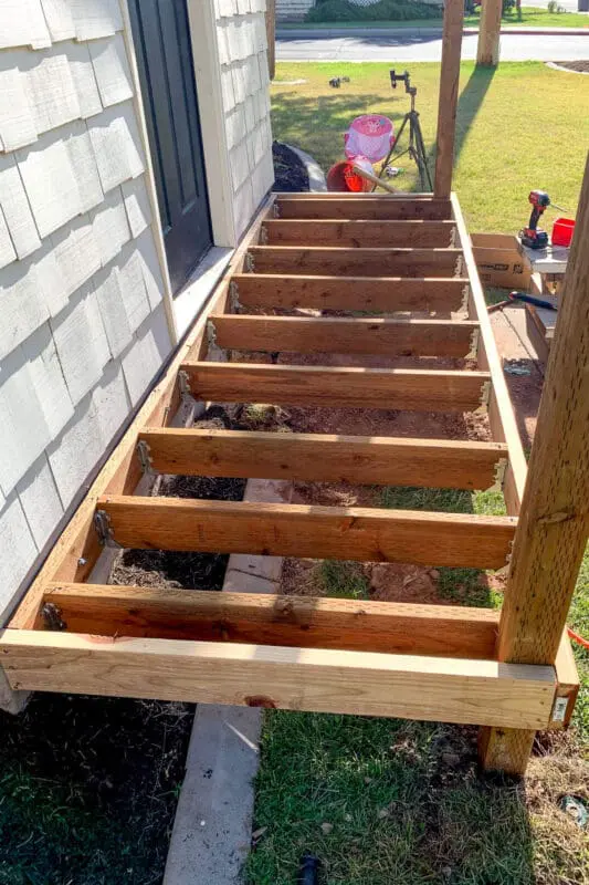 Top-down view of finished porch frame with pressure-treated joists evenly spaced and secured with joist hangers.