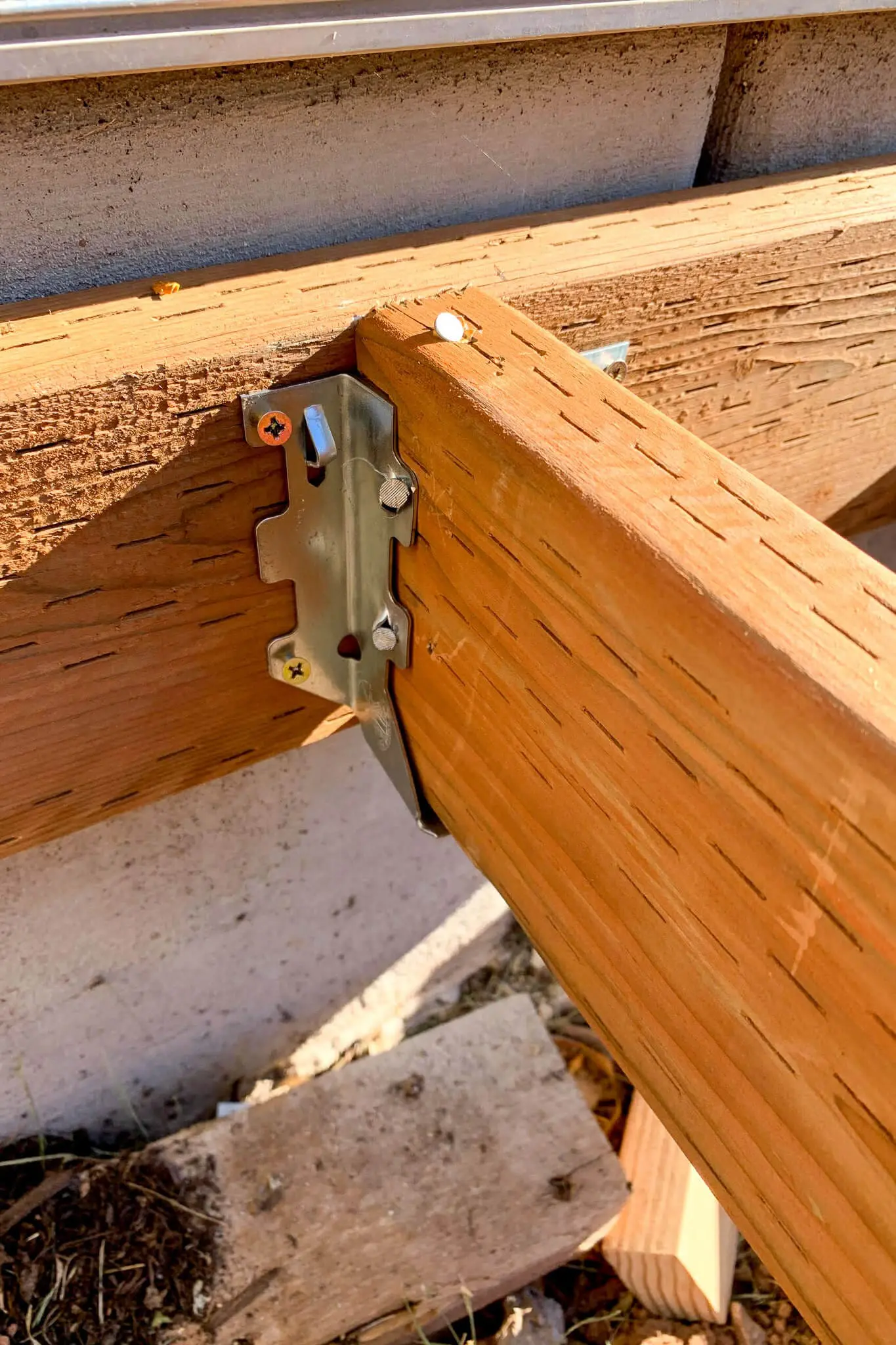 Close-up view of a metal joist hanger securing a pressure-treated 2x6 deck joist to a ledger board on a DIY front porch frame.