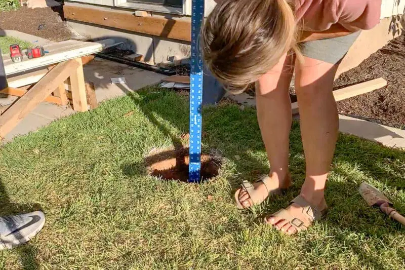 Woman measuring post hole depth with blue ruler during DIY front porch construction