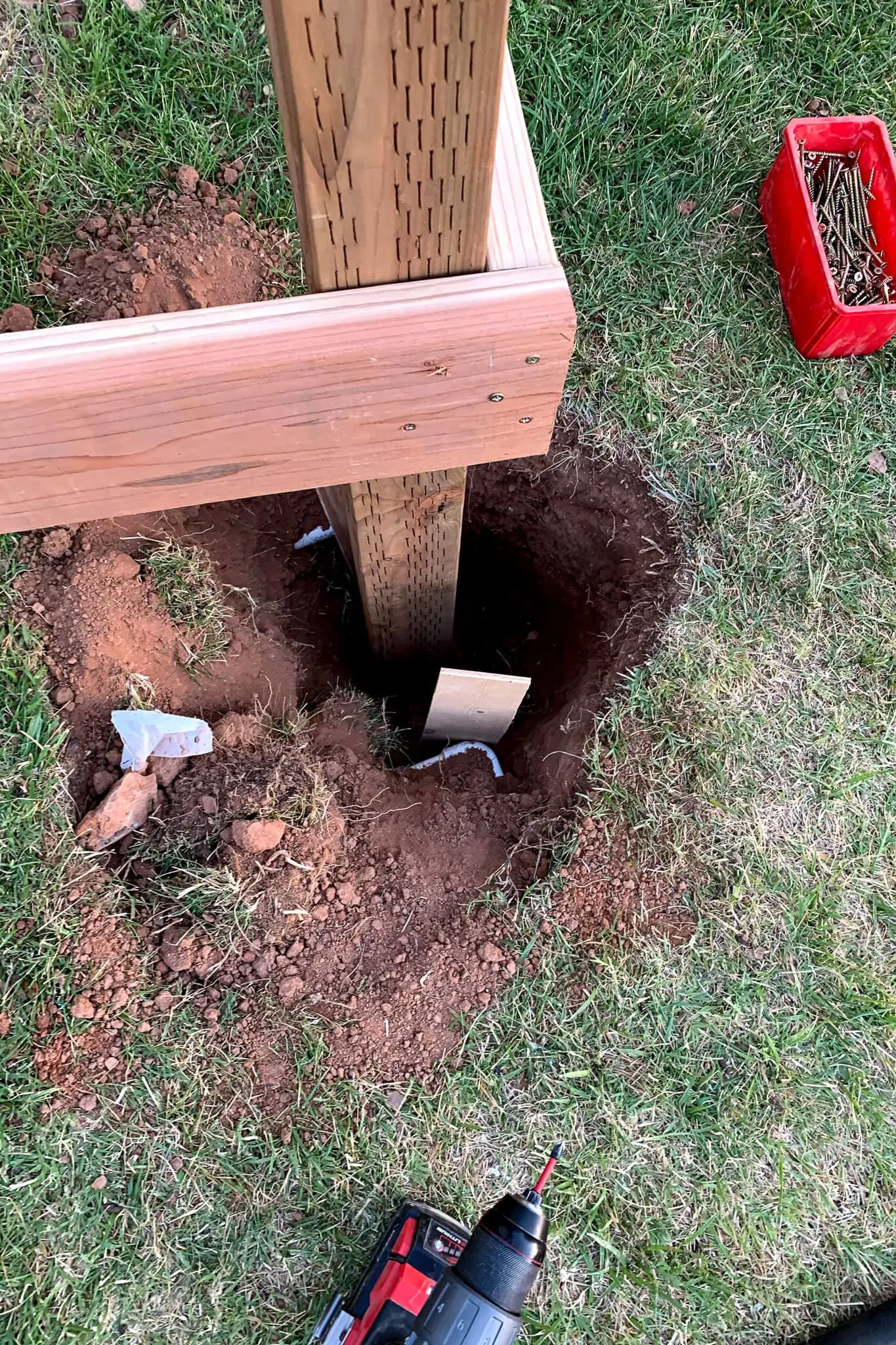 Top-down view of a 4x4 deck post set inside a deep hole, ready for concrete pour with framing brackets visible.