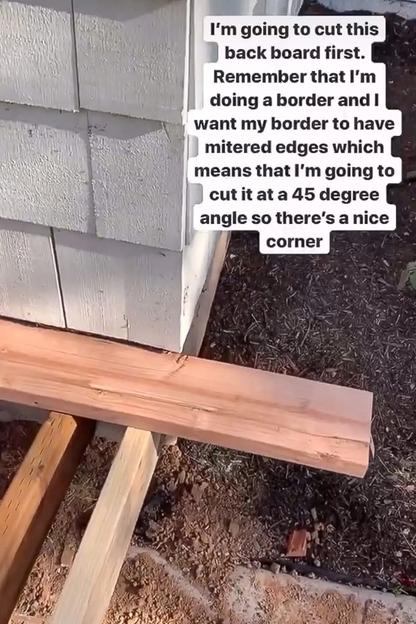 Wood board being measured and prepared with a 45-degree miter cut for the border trim on a front porch, with construction progress visible beneath.