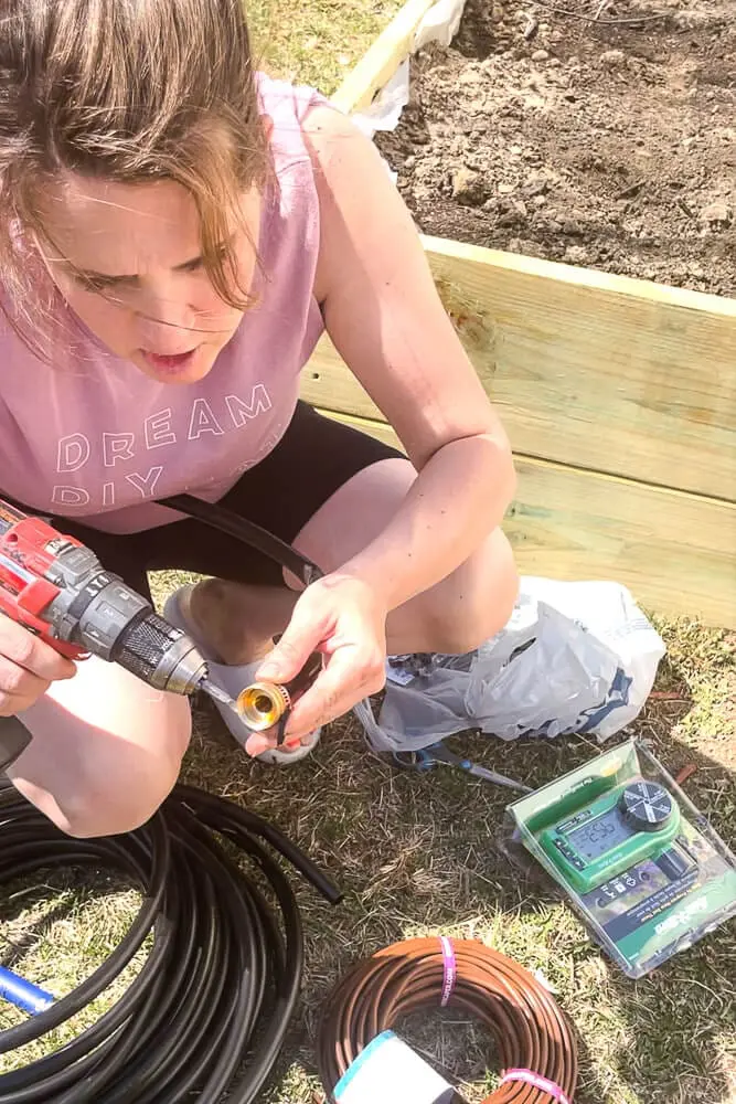 Woman using drill to secure clamp on irrigation tubing for homemade garden hose