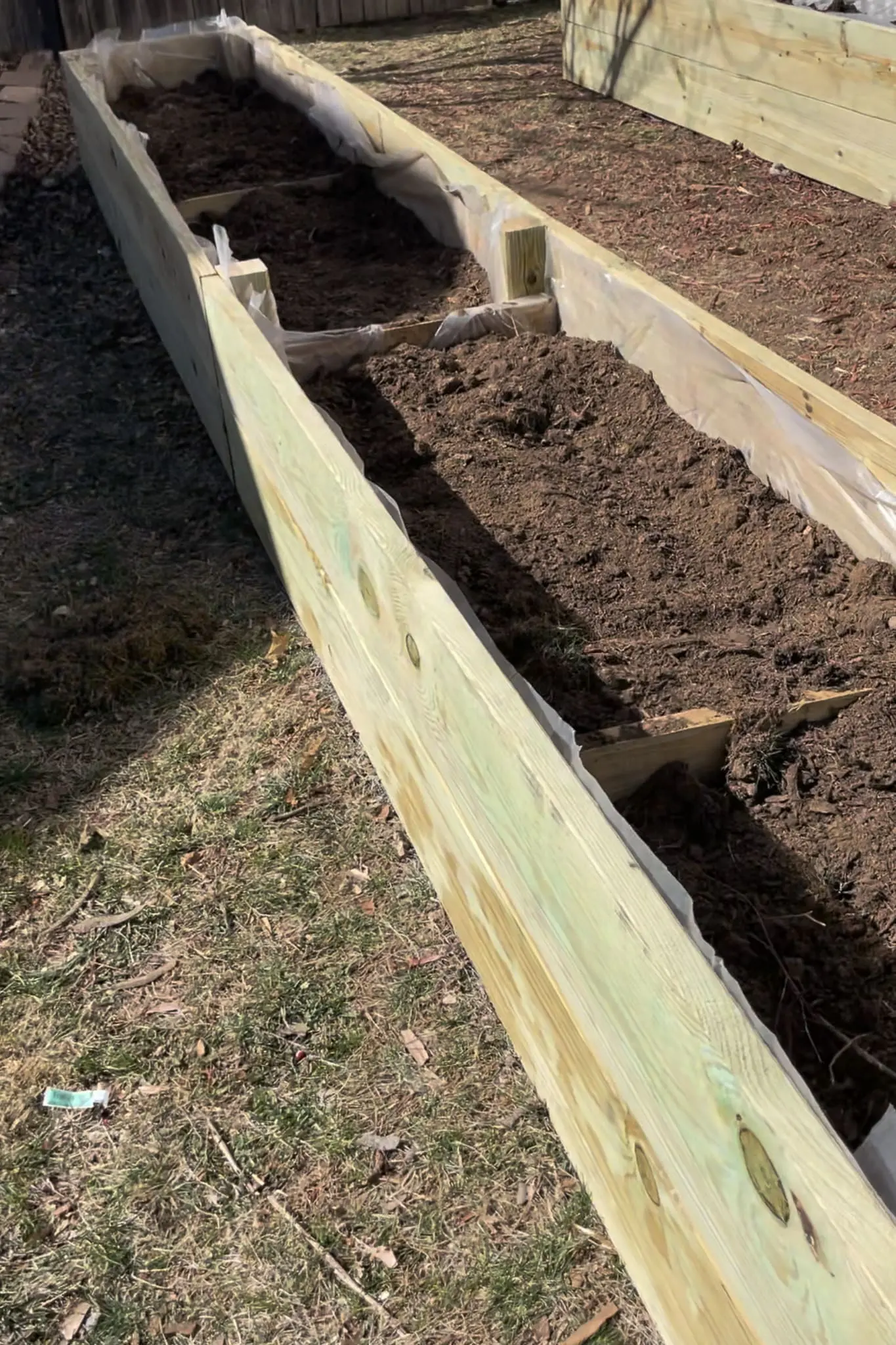 Overhead view of a backyard raised vegetable garden featuring tall wooden planter boxes filled with rich soil and thriving leafy plants.