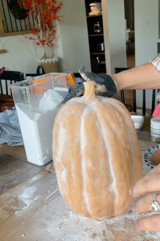 Hands applying baking soda mixture onto a pumpkin to create a faux terracotta textured finish for fall decor.