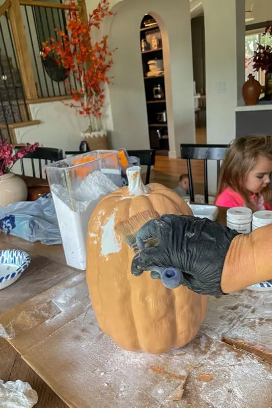 Painting a pumpkin with a baking soda paint mixture as a budget-friendly DIY fall decor hack.