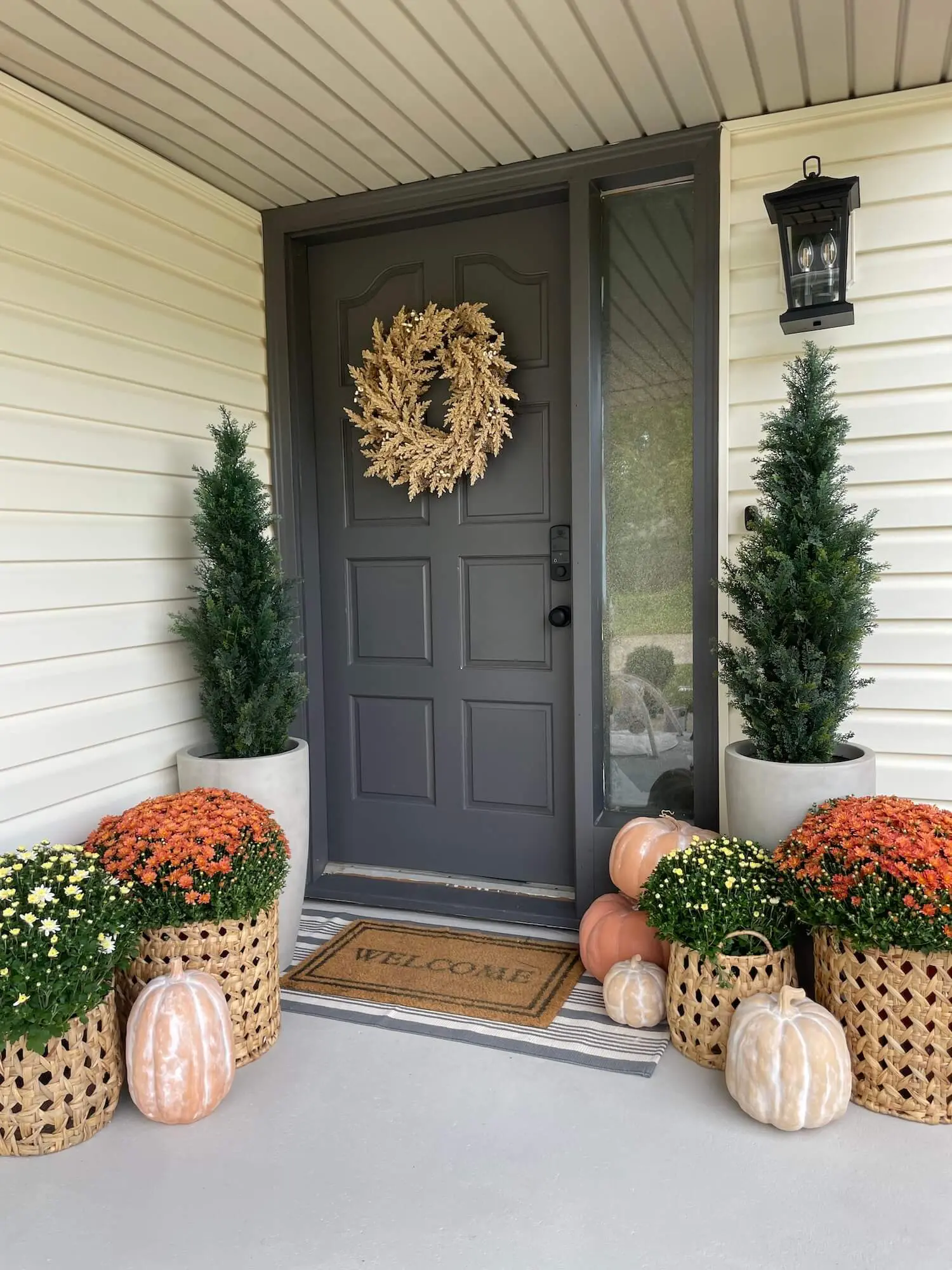 Neutral front porch decorated with faux terracotta pumpkins, mums, and woven baskets for autumn.