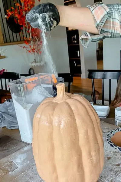 Hand sprinkling baking soda over wet paint on a pumpkin to achieve a rustic terracotta effect.