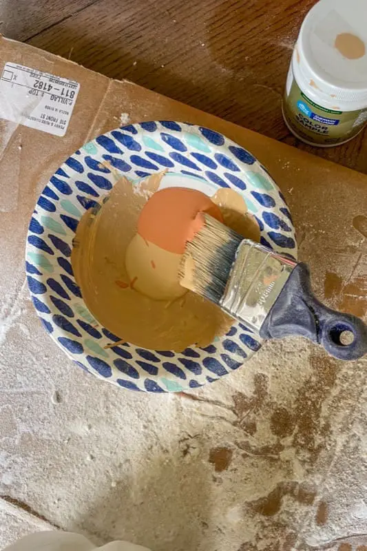 Bowl of tan and terracotta paint mixture with a brush used for painting pumpkins.
