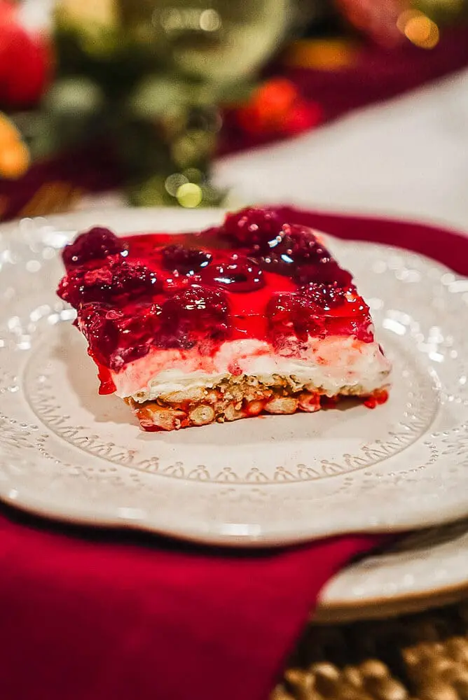 A slice of raspberry pretzel pie on a white plate, featuring layers of pretzel crust, creamy filling, and raspberry gelatin topping.