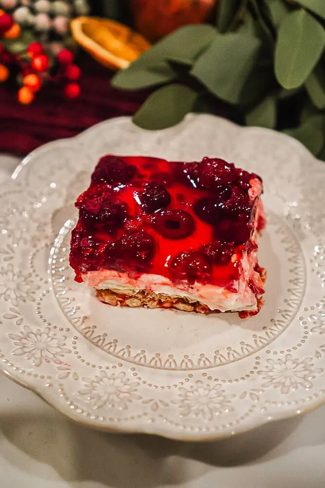 Close-up of raspberry pretzel pie with vibrant red raspberries suspended in gelatin, atop a creamy layer and crunchy pretzel crust.