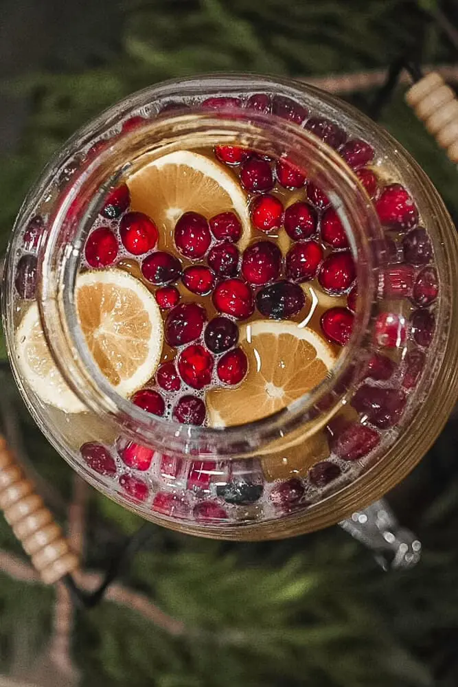 Top-down view of Lolly's Gold Punch in a glass dispenser, featuring floating cranberries and lemon slices for a festive touch.