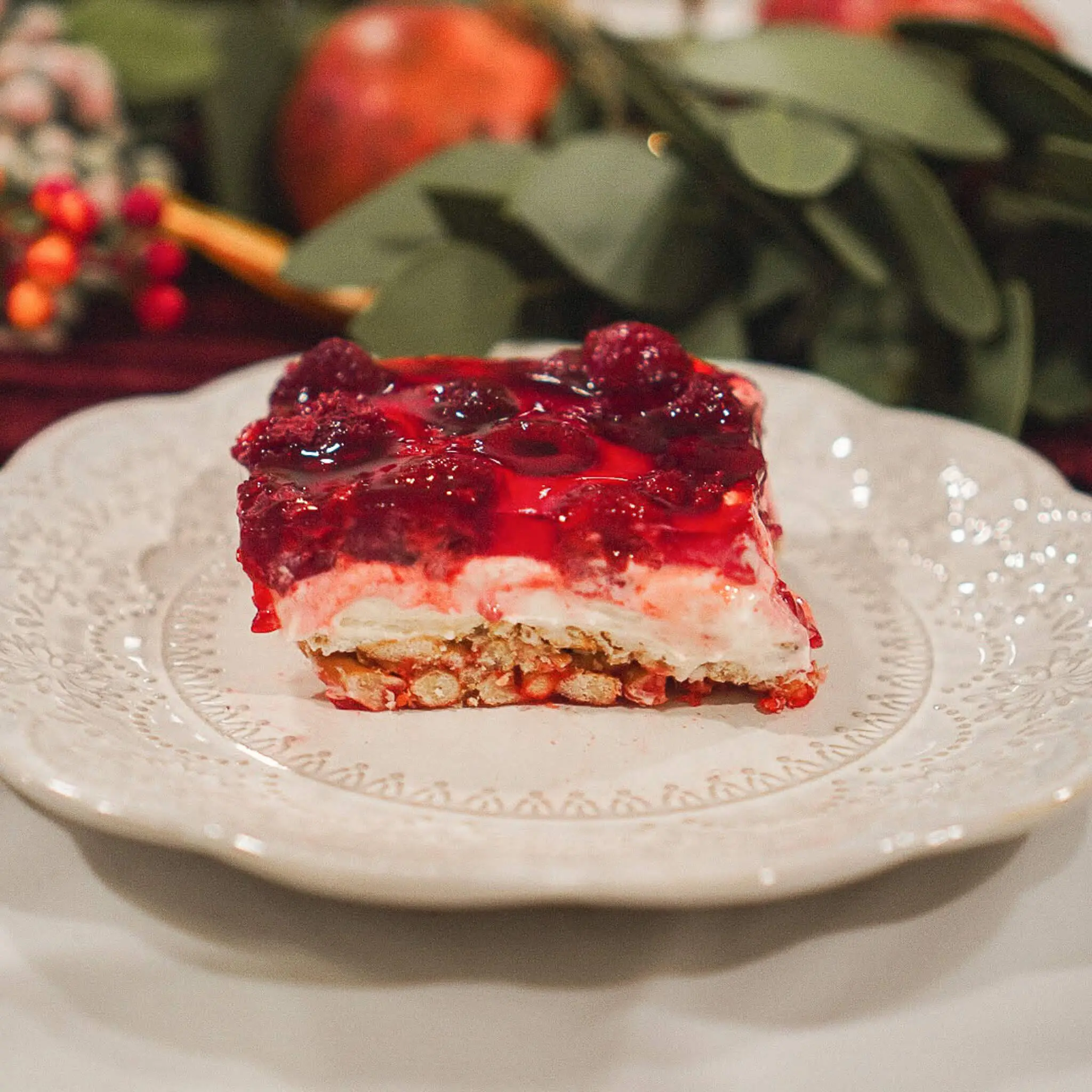 A slice of raspberry pretzel pie on a decorative plate, showing distinct layers of salty pretzel crust, creamy filling, and vibrant raspberry gelatin topping—perfect for holidays or potlucks.