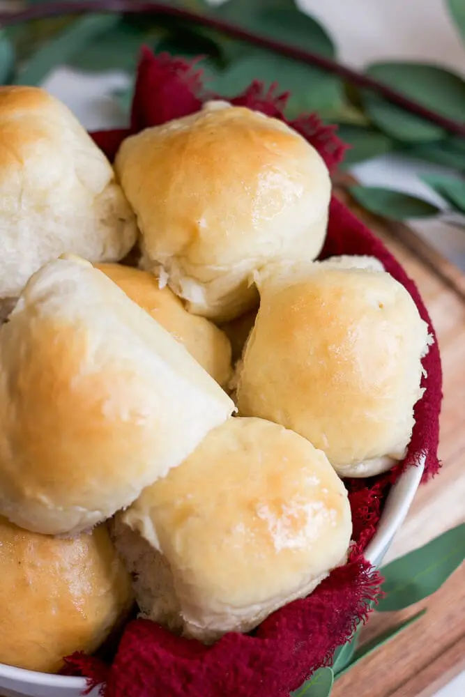 Close-up of fluffy, golden dinner rolls, glistening with a light buttery finish and resting in a red cloth.