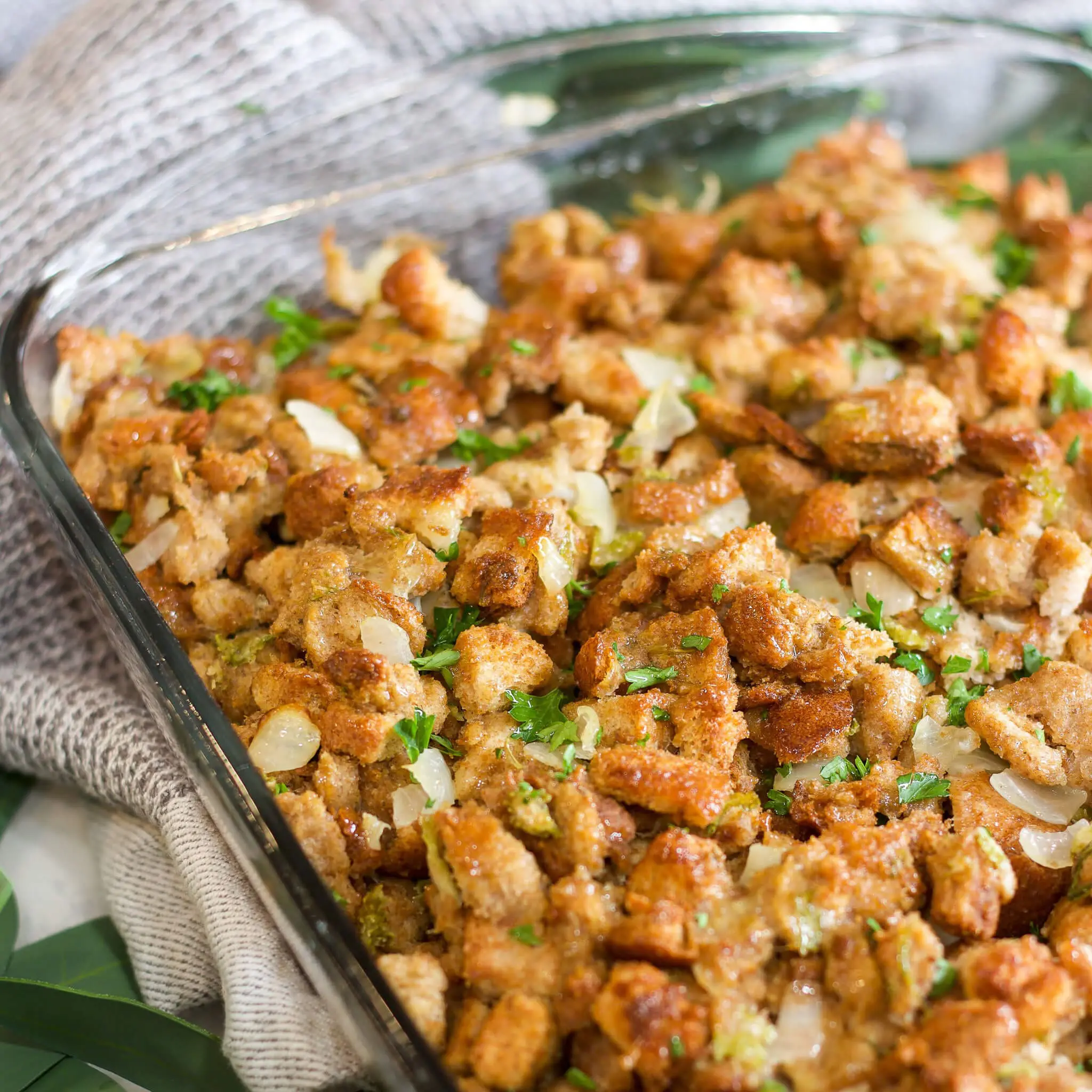 Golden brown Thanksgiving stuffing baked in a glass casserole dish, filled with cubed bread, sautéed onions, and herbs—perfect holiday side dish for your Thanksgiving table.