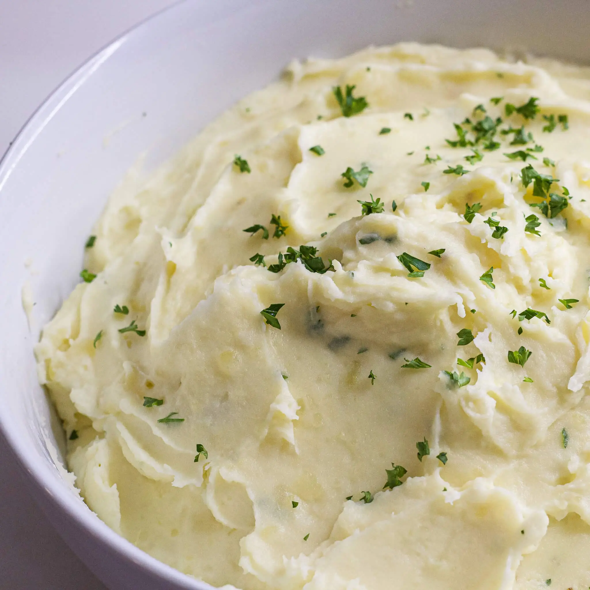 A white bowl filled with creamy garlic mashed potatoes, topped with freshly chopped parsley, showcasing the smooth texture and rich, buttery consistency—perfect for holiday meals or cozy dinners. Let me know if you'd like a Pinterest caption or a social media description too!
