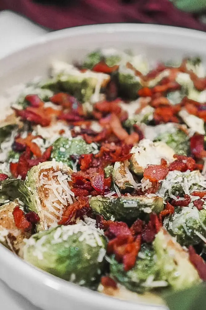 A serving dish with Brussels sprouts topped with crispy bacon and Parmesan