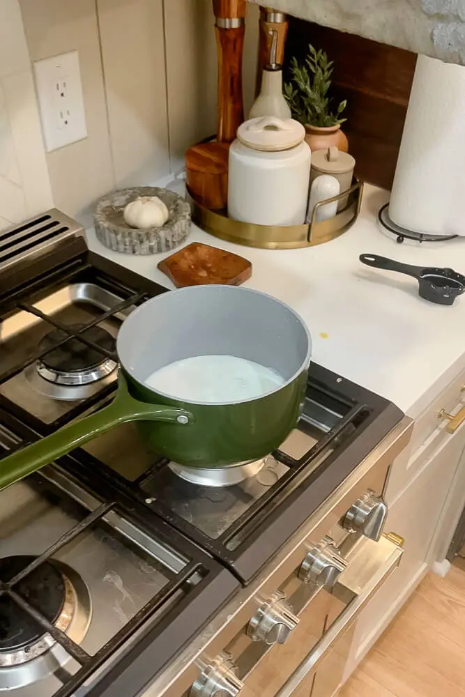 A green saucepan on the stovetop with milk warming, a step in preparing dough for the perfect dinner rolls.