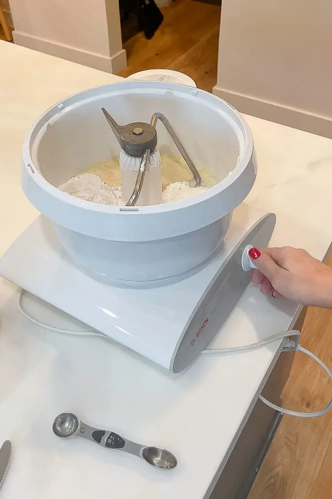 Flour and ingredients being mixed in a stand mixer to create dough for dinner rolls.